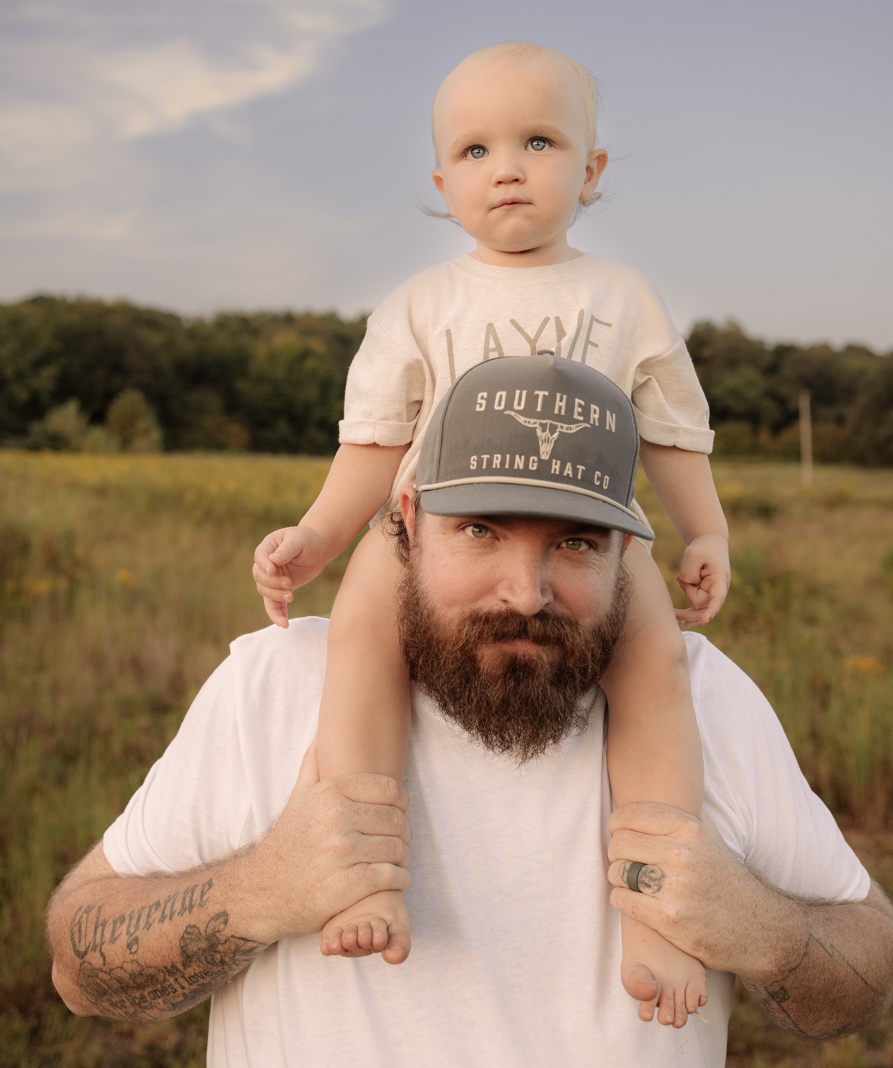 A toddler riding on dad’s shoulders in a sunlit field